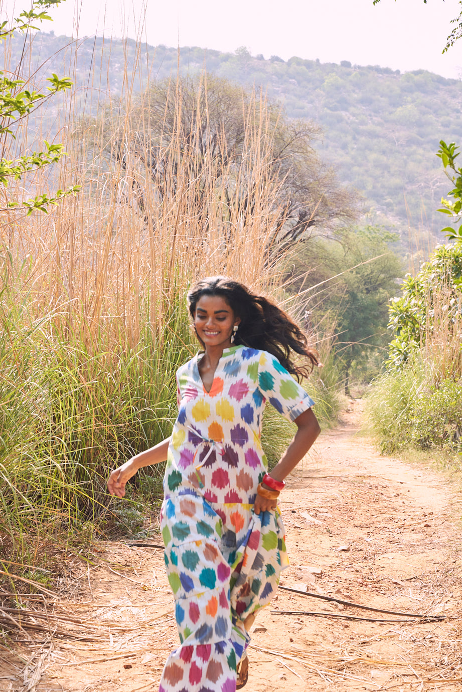 editorial photo of model wearing anouk maxi dress by kleed in 100% cotton ikat. Running in the countryside. 