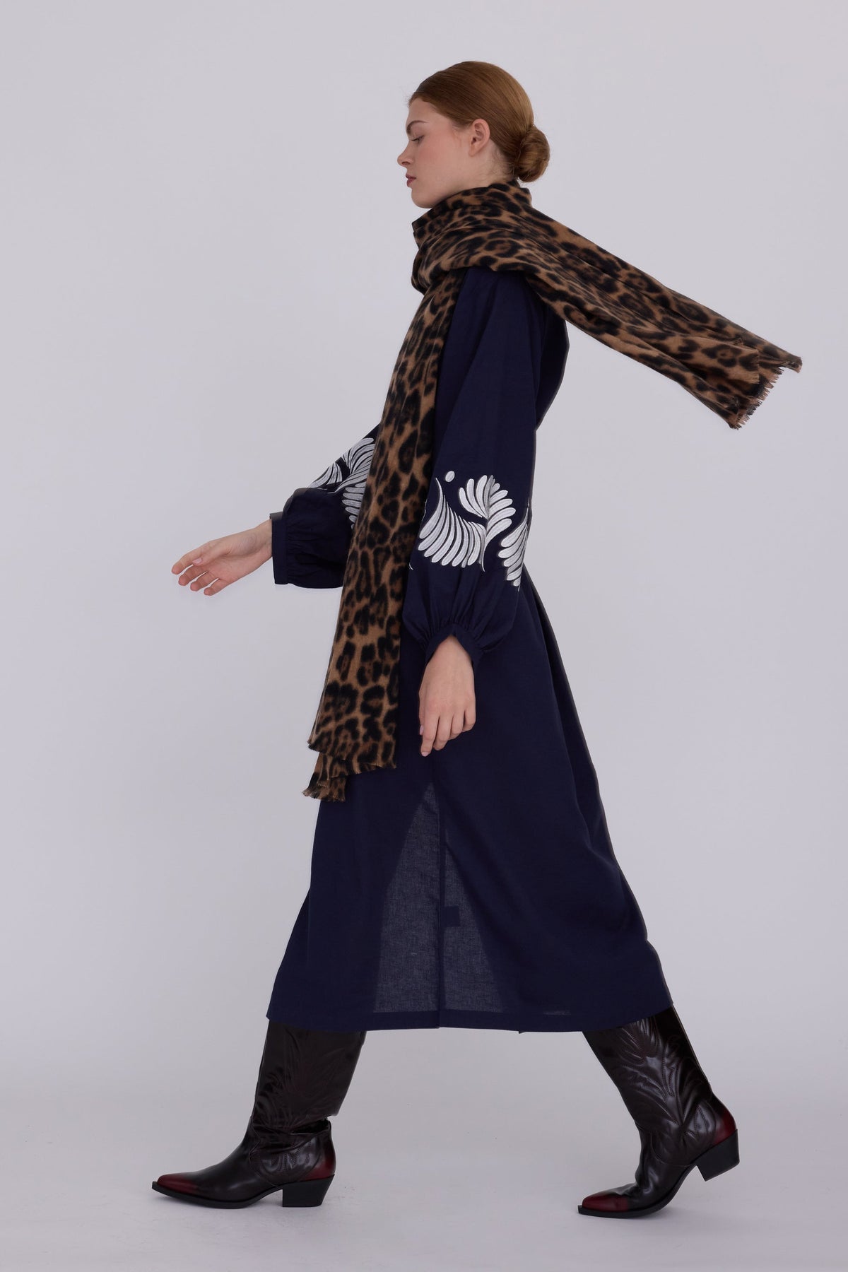 Woman walking wearing Kleed Blue Kandy Kimono in 100% cotton dark navy blue white floral embroidered cuffs styled with leopard print scarf and cowboy boots