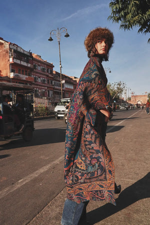 Woman wearing Kleed Fuchsia Paisley Kimono Coat in wool on a sunlit street, long paisley print coat with belt.
