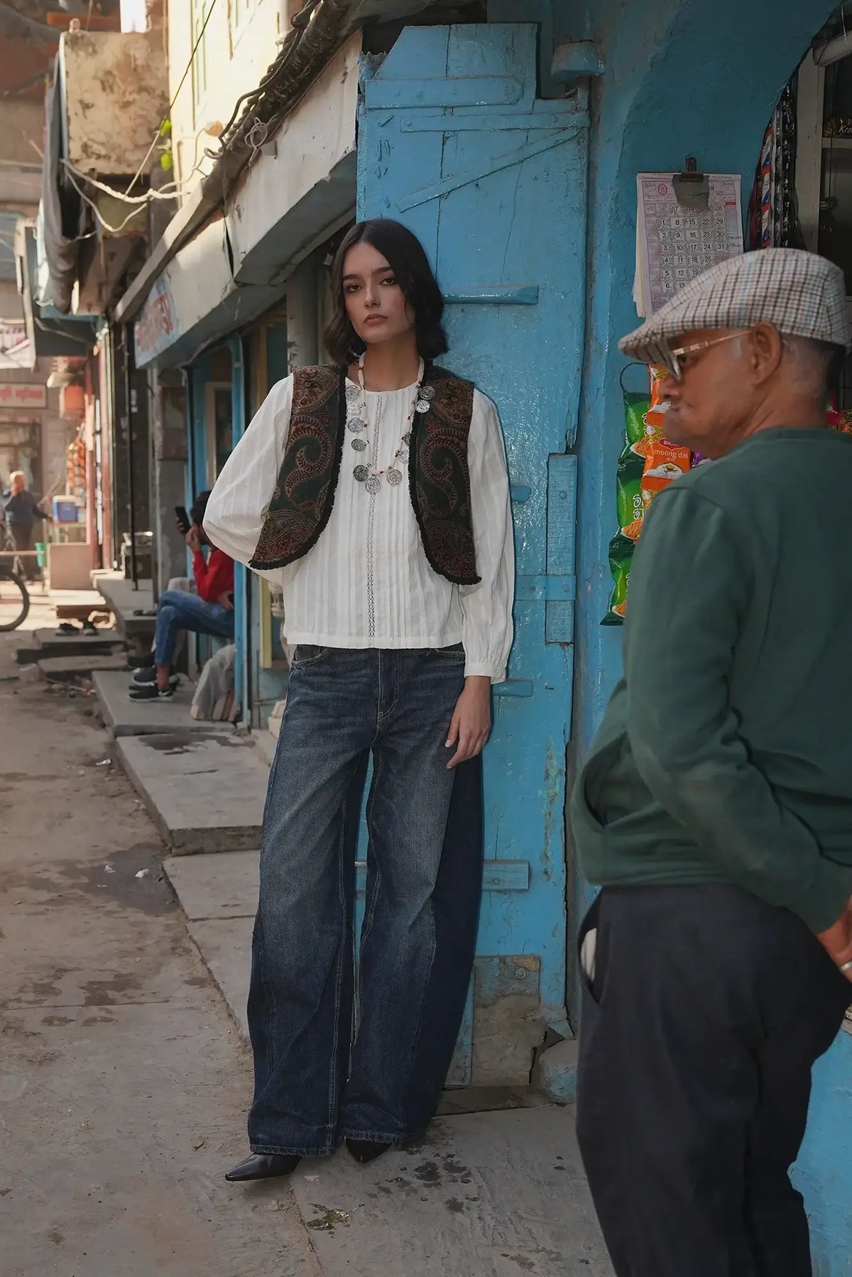 Model standing on a blue painted street wearing Kleed Green Oak Vest in wool with paisley swirls and frayed trim.