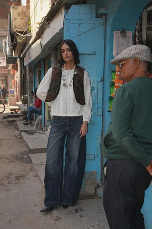 Model standing on a blue painted street wearing Kleed Green Oak Vest in wool with paisley swirls and frayed trim.