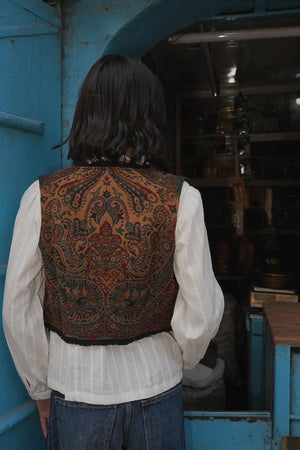 Model from behind wearing Kleed Green Oak Vest in pure wool, paisley print on the back over a white blouse.
