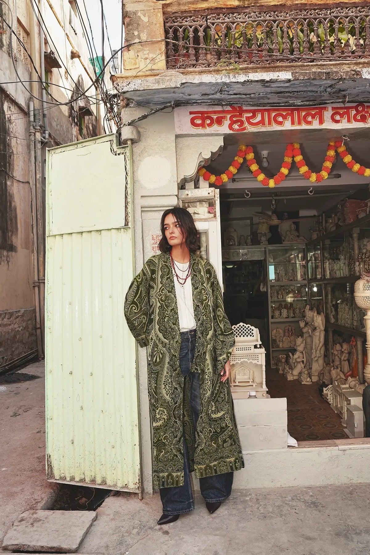 Full length front view of a woman wearing the Kleed Green Paisley Wool Kimono Coat styled with wide leg jeans in an outdoor street setting
