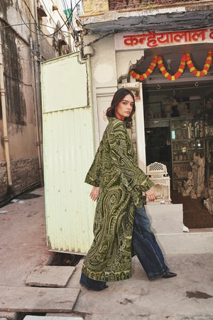 Full length side view of a woman wearing the Kleed Green Paisley Wool Kimono Coat in an outdoor street setting