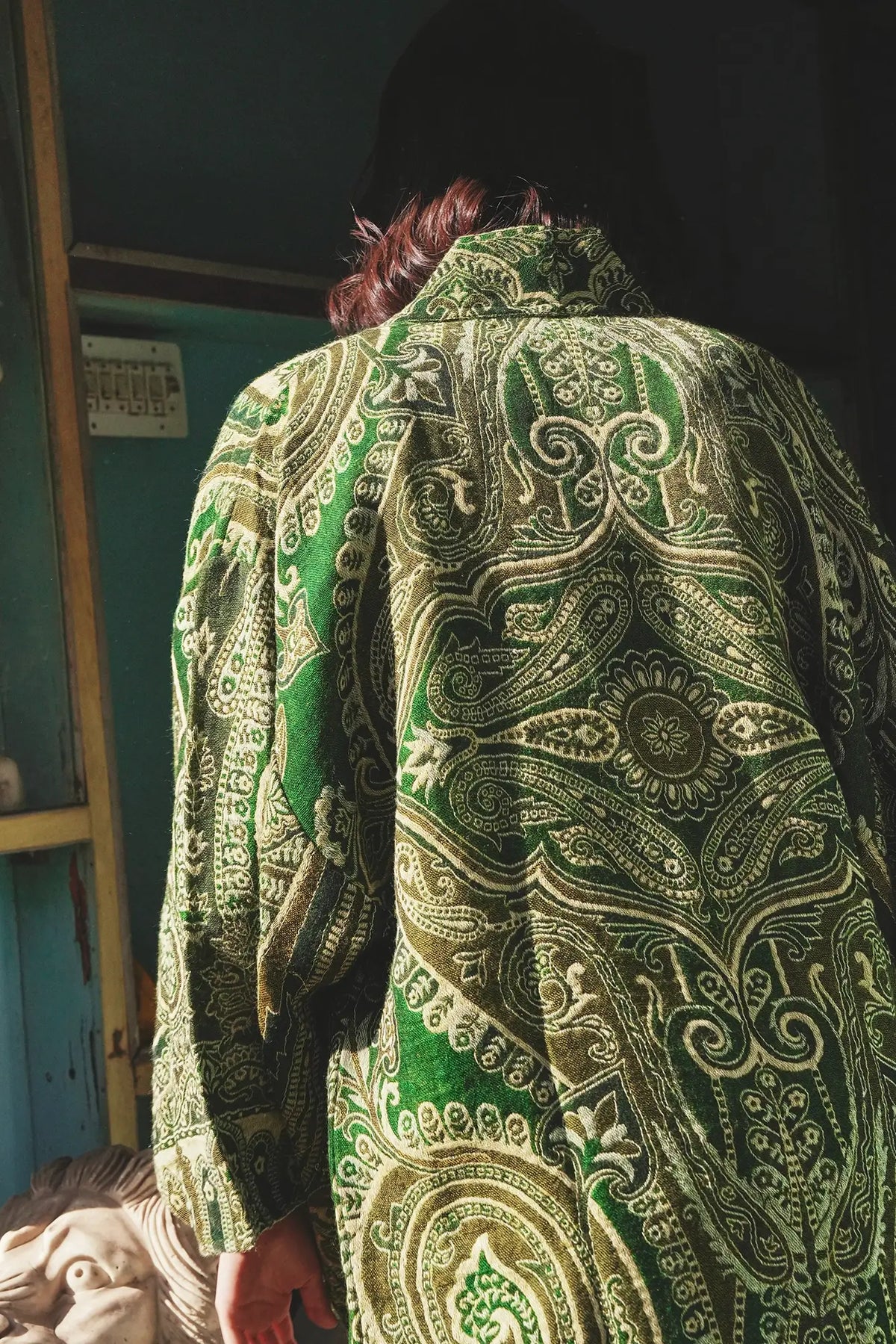 Back view close up of the Kleed Green Paisley Wool Kimono Coat showing the vibrant handcrafted green and gold paisley pattern, photographed in an indoor artisan setting