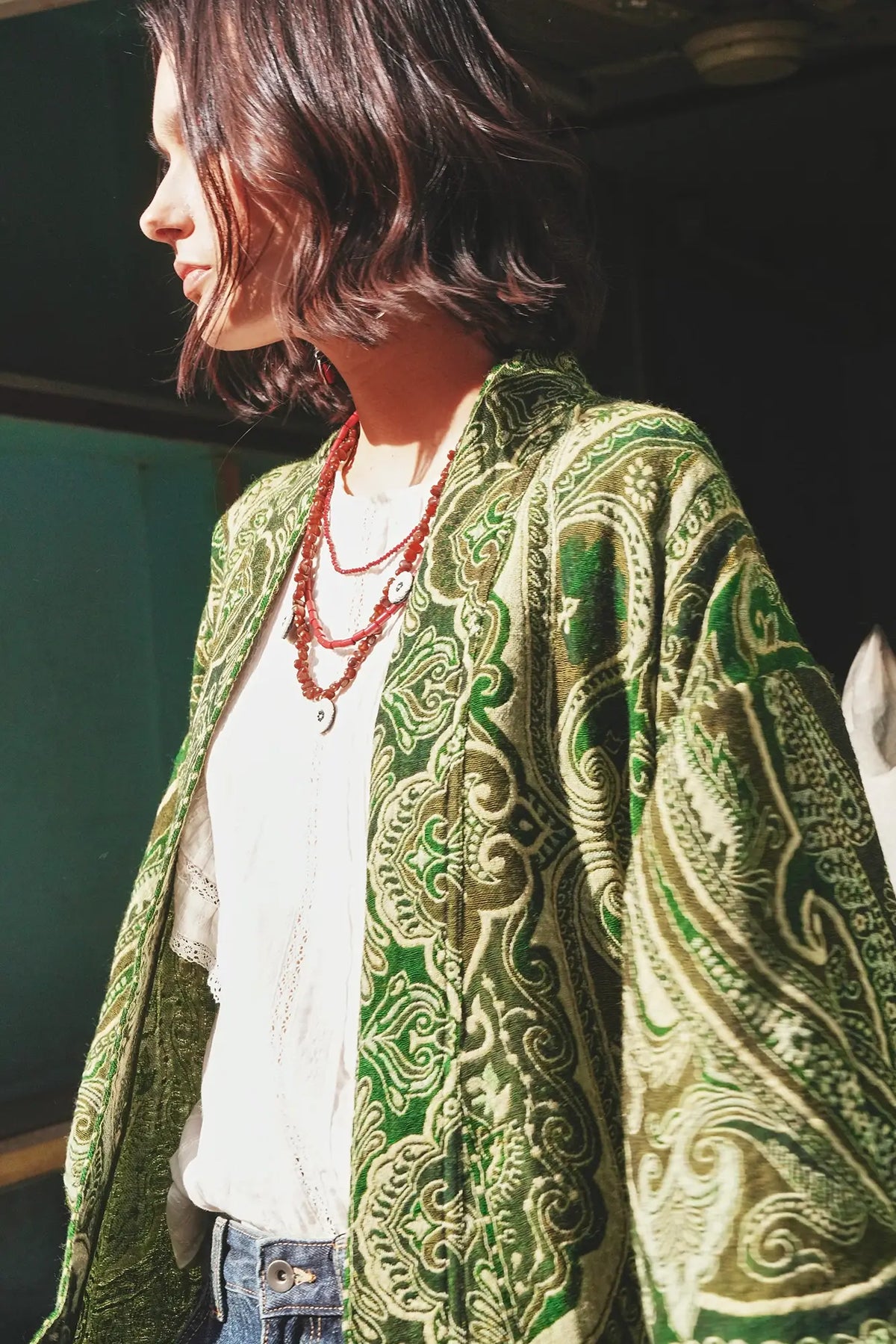 Close up detail of the Kleed Green Paisley Wool Kimono Coat showing the handcrafted green and gold paisley pattern, styled with a pink beaded necklace