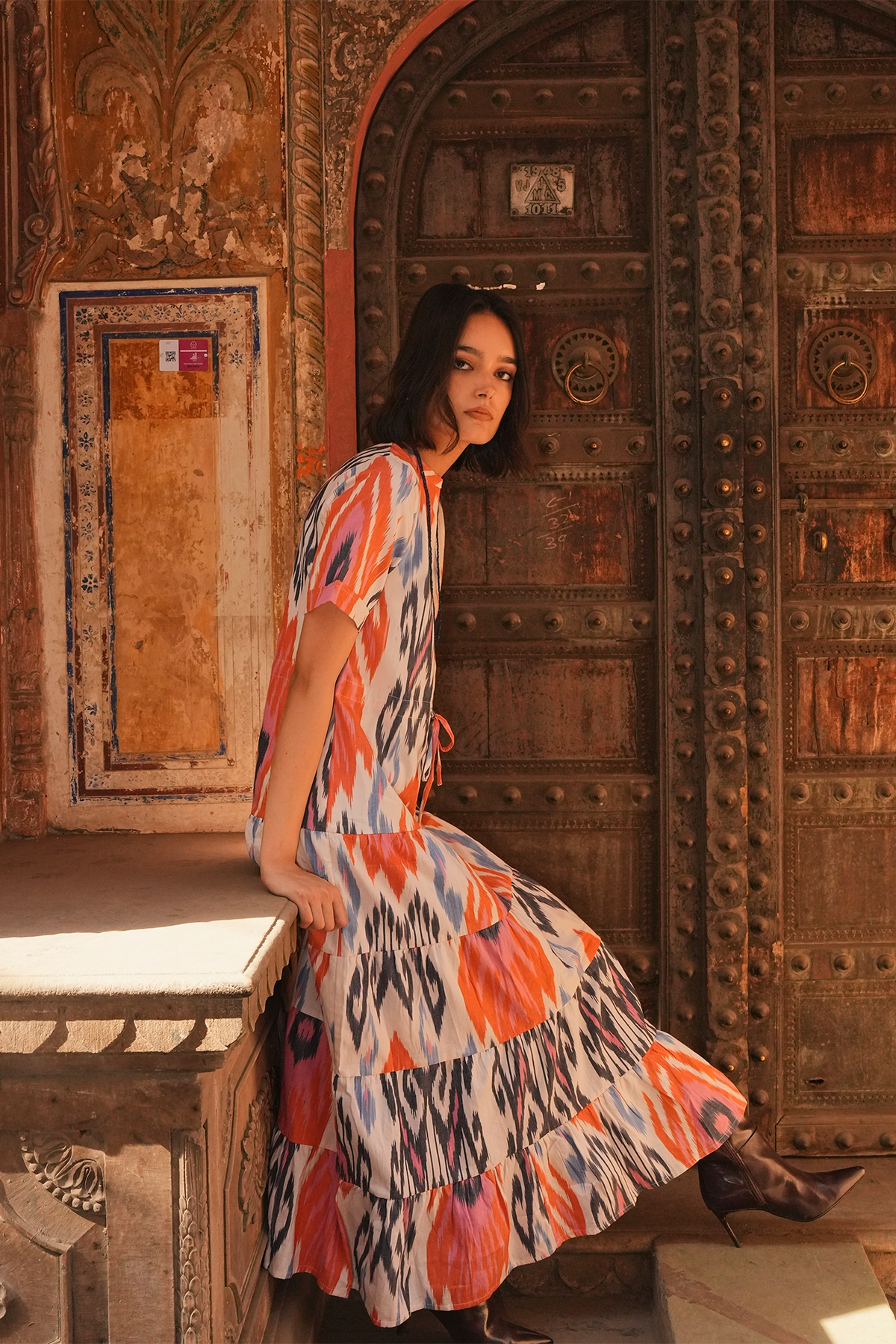Full length view of a woman wearing the Kleed Tangerine Bikaner Maxi Dress in handloomed cotton ikat, standing in front of a carved wooden doorway