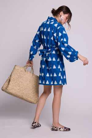 Model from behind wearing Kleed Turquoise Savannah Short Kimono in handwoven Ikat cotton tied at the waist, holding a large straw tote.
