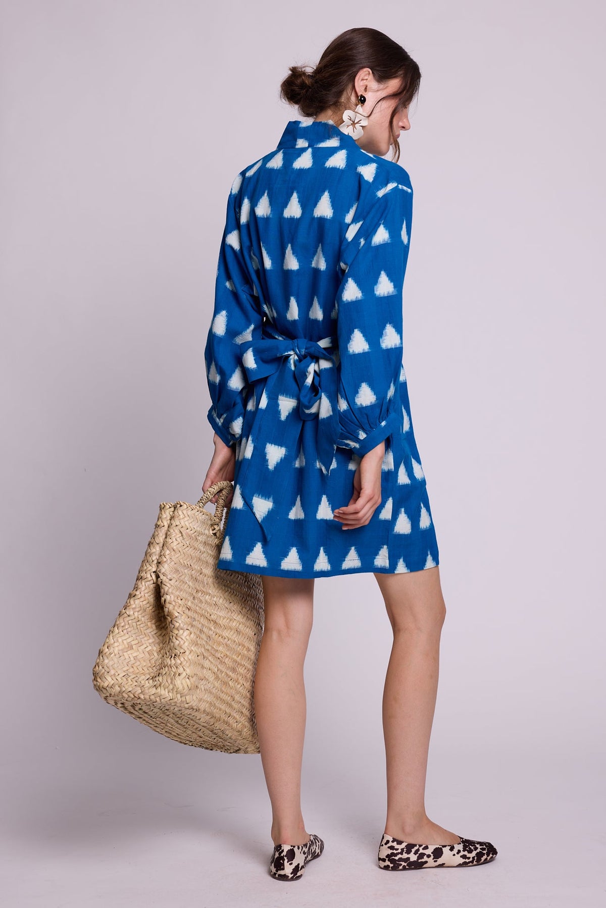 Model wearing Kleed Turquoise Savannah Short Kimono in handwoven Ikat cotton with balloon sleeves and matching belt, with a straw tote.