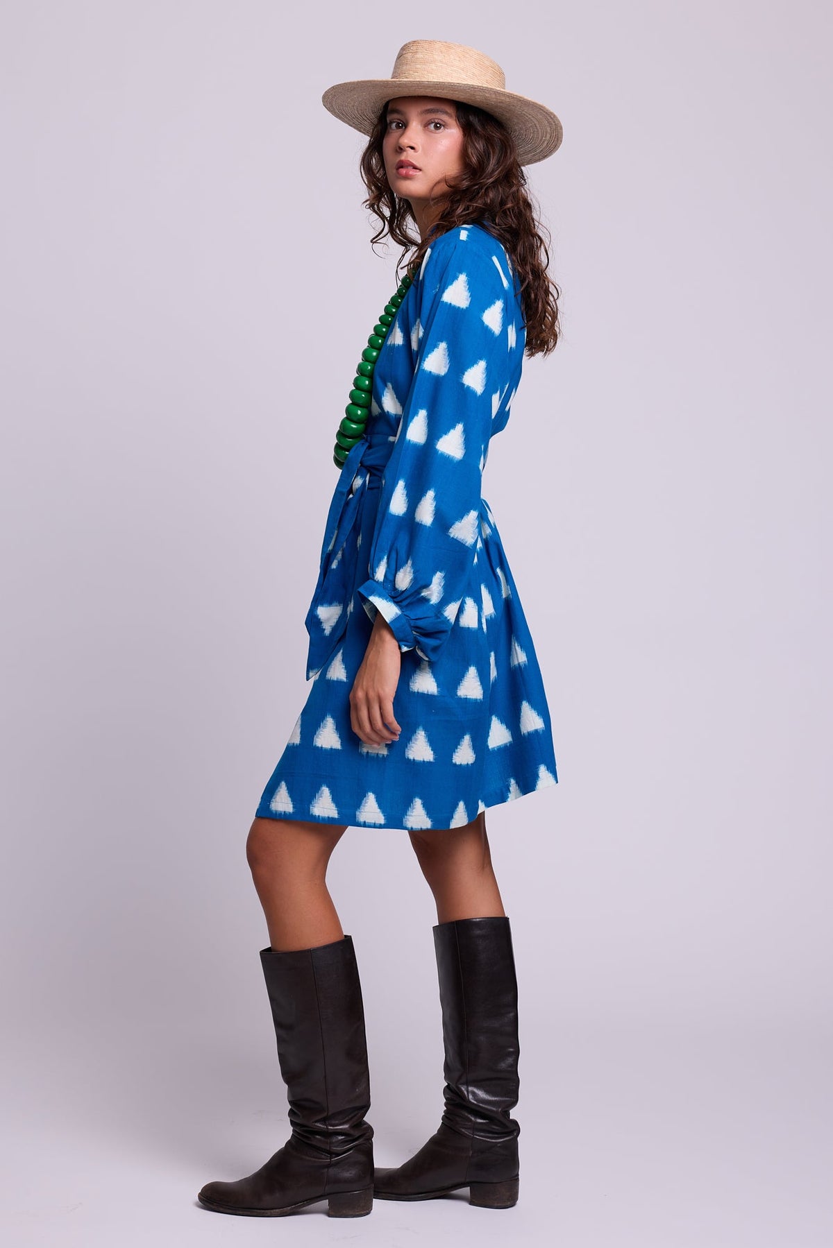 Model standing in profile wearing Kleed Turquoise Savannah Short Kimono in Ikat cotton, styled with a straw hat and black knee-high boots.