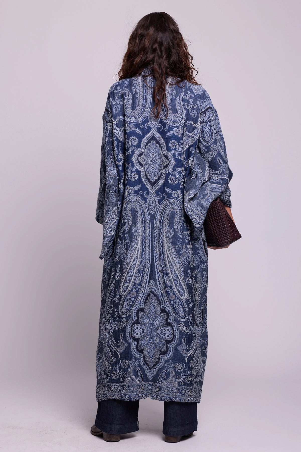 Back view of Kleed Blue Paisley Kimono Coat in pure wool with indigo paisley print, styled with dark jeans and a woven leather clutch.