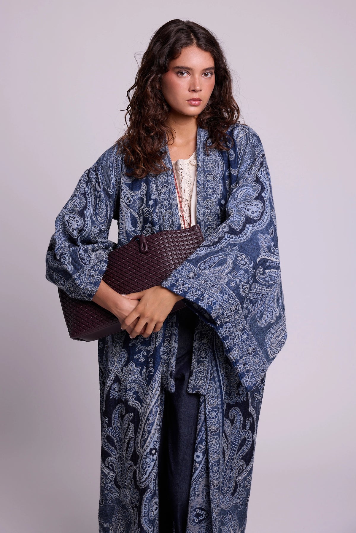 Kleed Blue Paisley Kimono Coat in pure wool with indigo paisley print, styled open over a white lace top with a woven leather clutch.