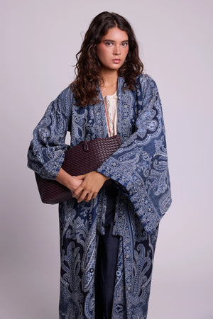 Kleed Blue Paisley Kimono Coat in pure wool with indigo paisley print, styled open over a white lace top with a woven leather clutch.