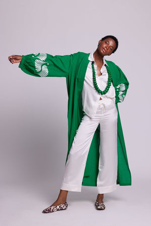 Woman wearing Kleed´s Green Kandy Kimono in 100% cotton with white floral embroidered sleeves, arms outstretched, styled with white silk pyjama, green beaded necklace and leopard print flat mules