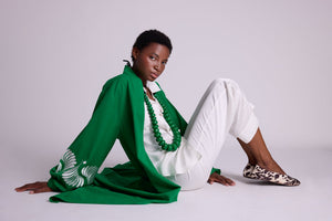 Woman seated on the floor wearing the Kleed Green Kandy Kimono in 100% cotton with white floral embroidered sleeves, styled with white silk pyjamas and green beaded necklace