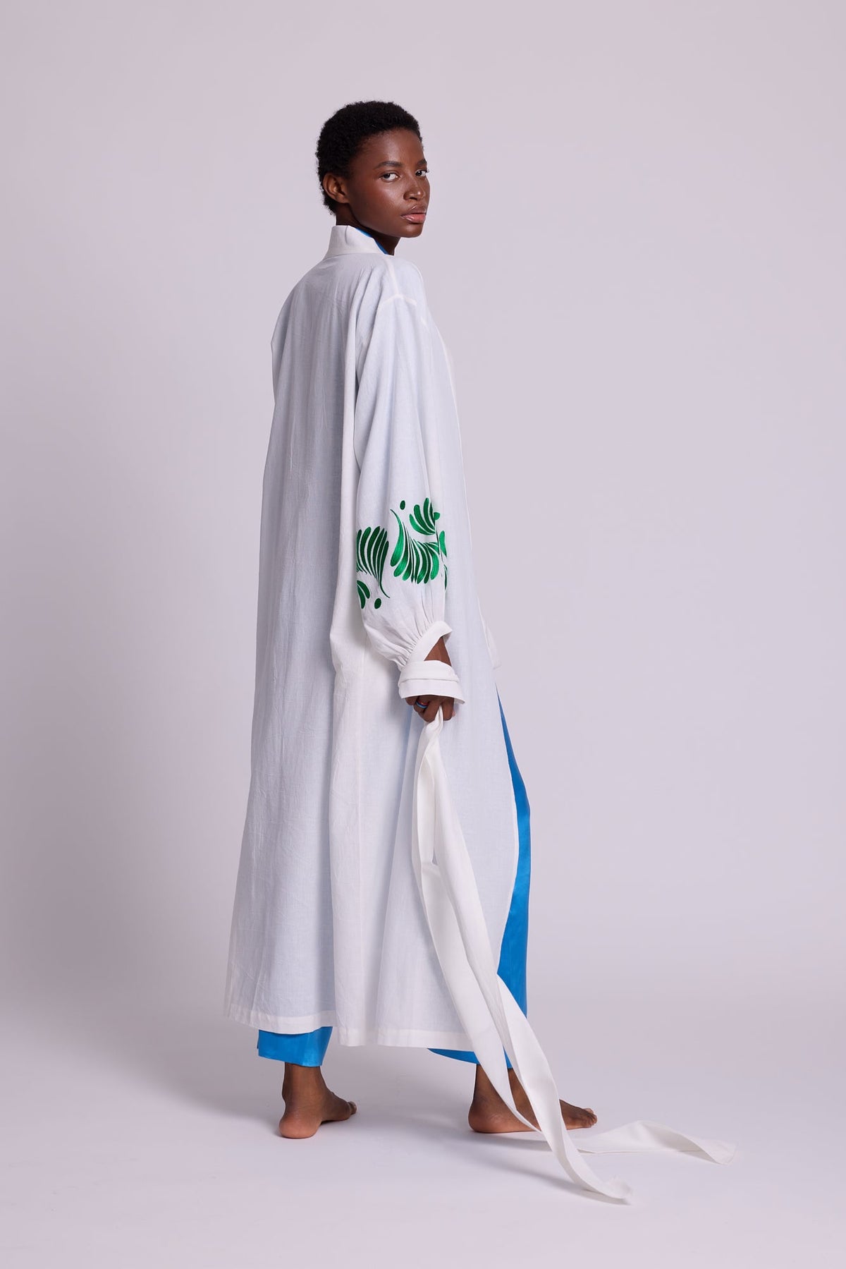 Side view of Kleed Light Kandy Kimono in white cotton with embroidered cuffs, worn over sky blue silk pyjama.