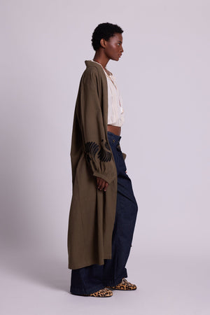 Side view of Kleed Olive Kandy Kimono in khaki cotton with black floral embroidery on cuffs, styled with white top and dark jeans.
