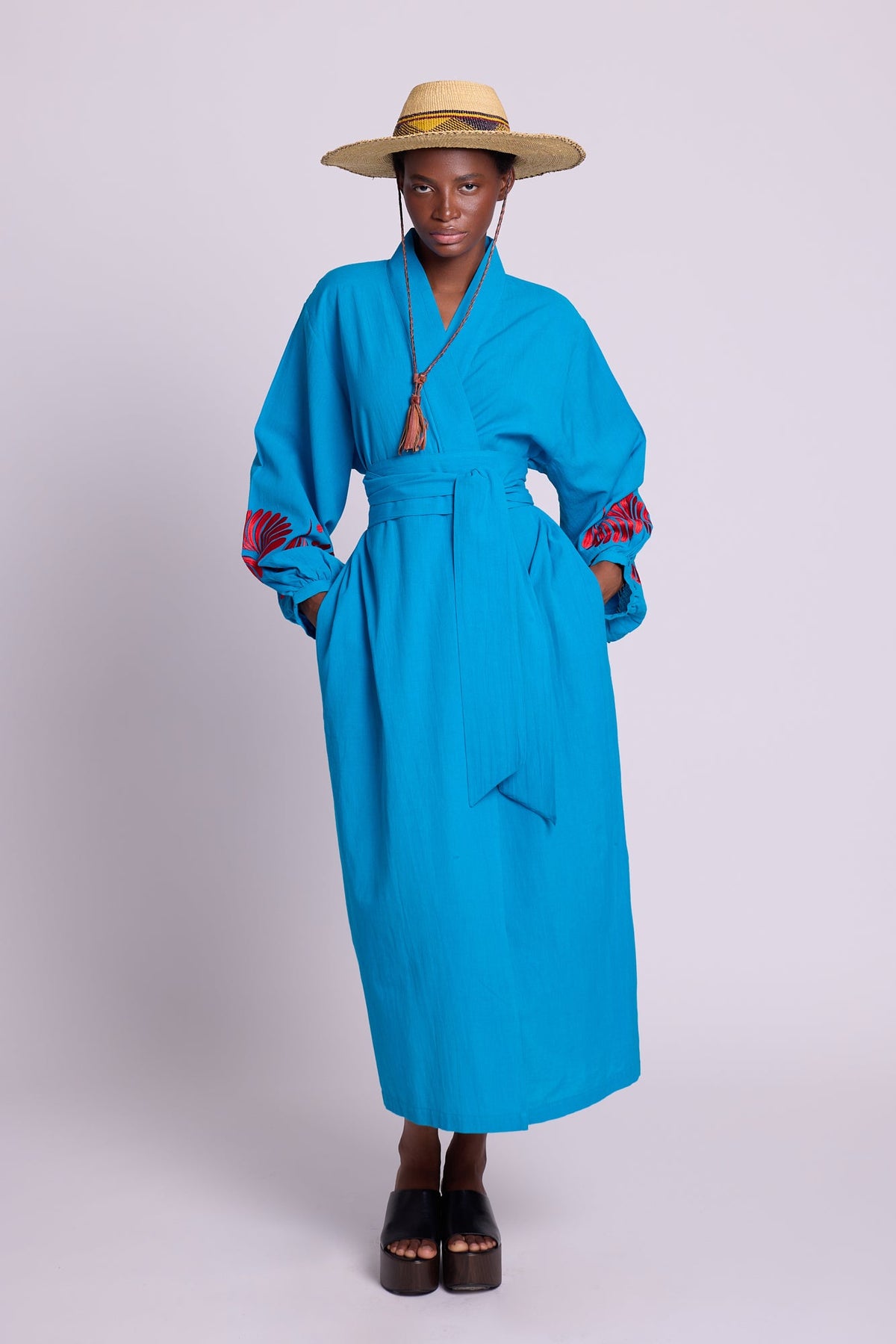 Woman wearing Kleed Sky Blue Kandy Kimono in cotton with red silk embroidery on cuffs, tied with a wide belt.