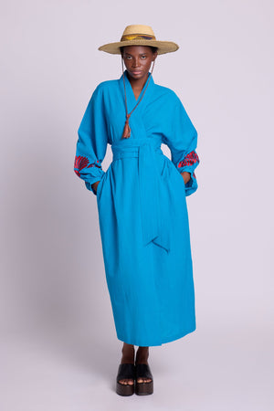 Woman wearing Kleed Sky Blue Kandy Kimono in cotton with red silk embroidery on cuffs, tied with a wide belt.