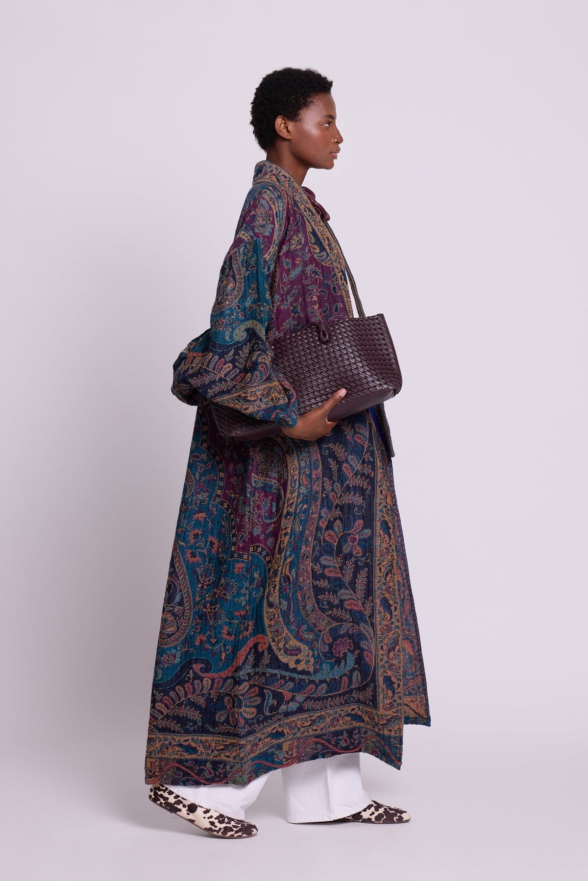 Side view of Kleed Fuchsia Paisley Kimono Coat in 100% wool, styled with white wide-leg trousers and a woven leather tote.