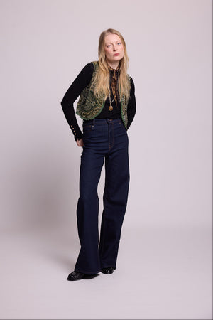 Full length view of a woman wearing the Kleed Green Paisley Wool Vest over a black top and dark wide leg jeans, alternative pose