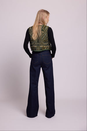 Full length bacj view of a woman wearing the Kleed Green Paisley Wool Vest over a black long sleeve top and dark wide leg jeans