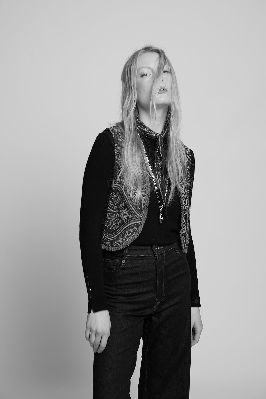 Black and white full length photo of a woman wearing the Kleed Green Paisley Wool Vest over a black long sleeve top