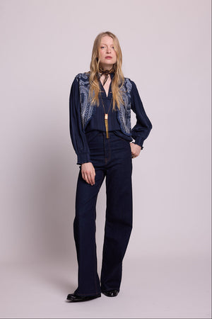 Full length front view of a woman wearing the Kleed Blue Paisley Vest over a navy blouse, styled with dark wide leg jeans, a dark neck scarf and a gold pendant necklace