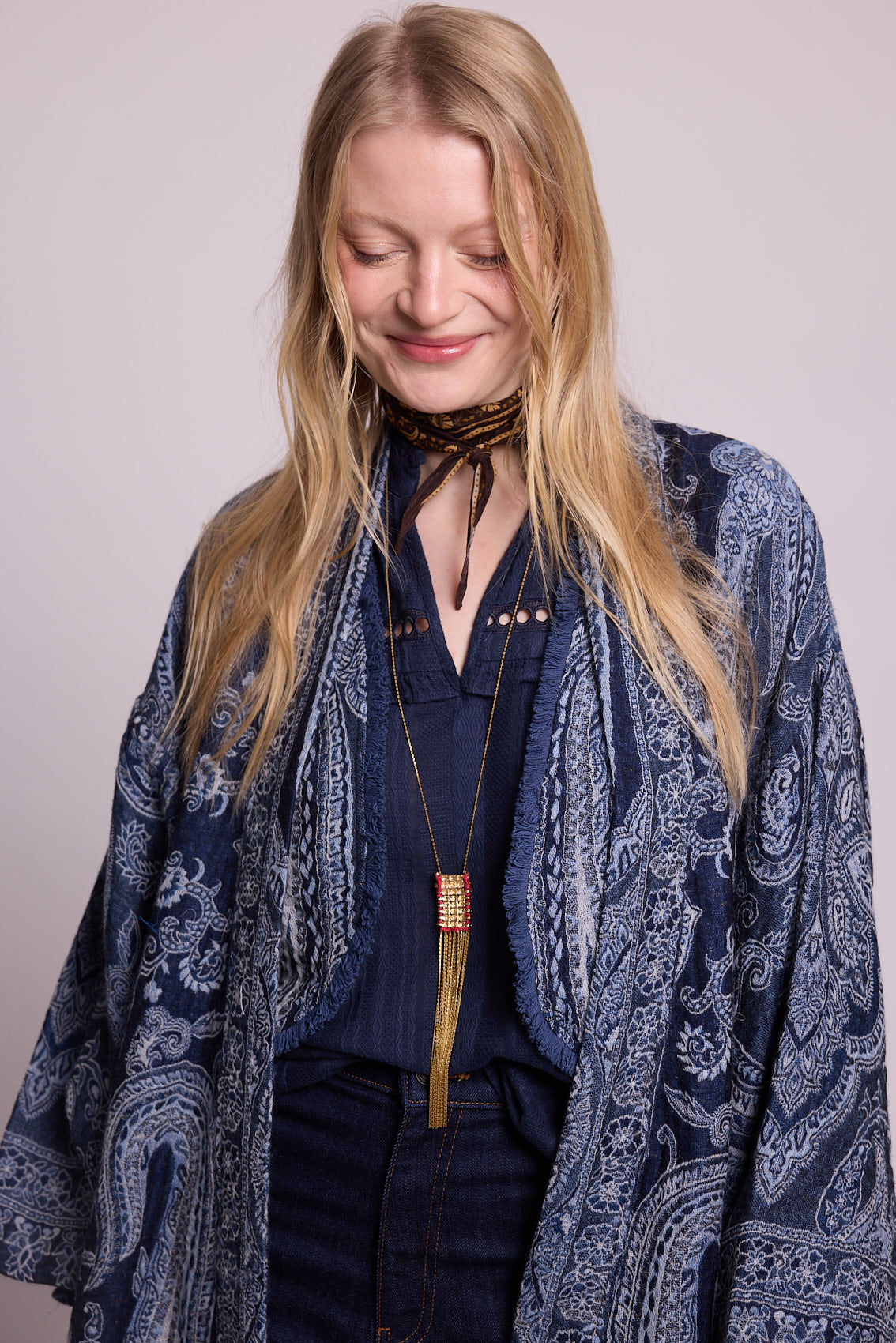 Woman smiling wearing the Kleed Blue Paisley Vest layered under a blue paisley kimono coat, styled with a navy blouse, dark wide leg jeans, dark neck scarf and gold tassel pendant necklace