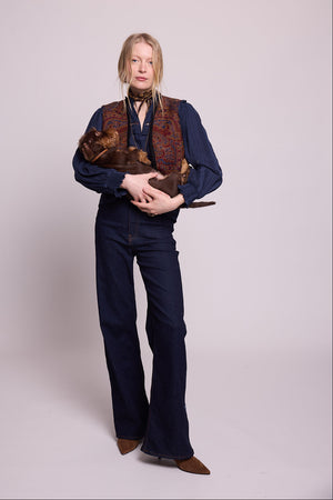 Model standing wearing Kleed Blue Oak Vest in wool with paisley print, navy balloon-sleeve blouse and dark wide-leg jeans, holding a dachshund.