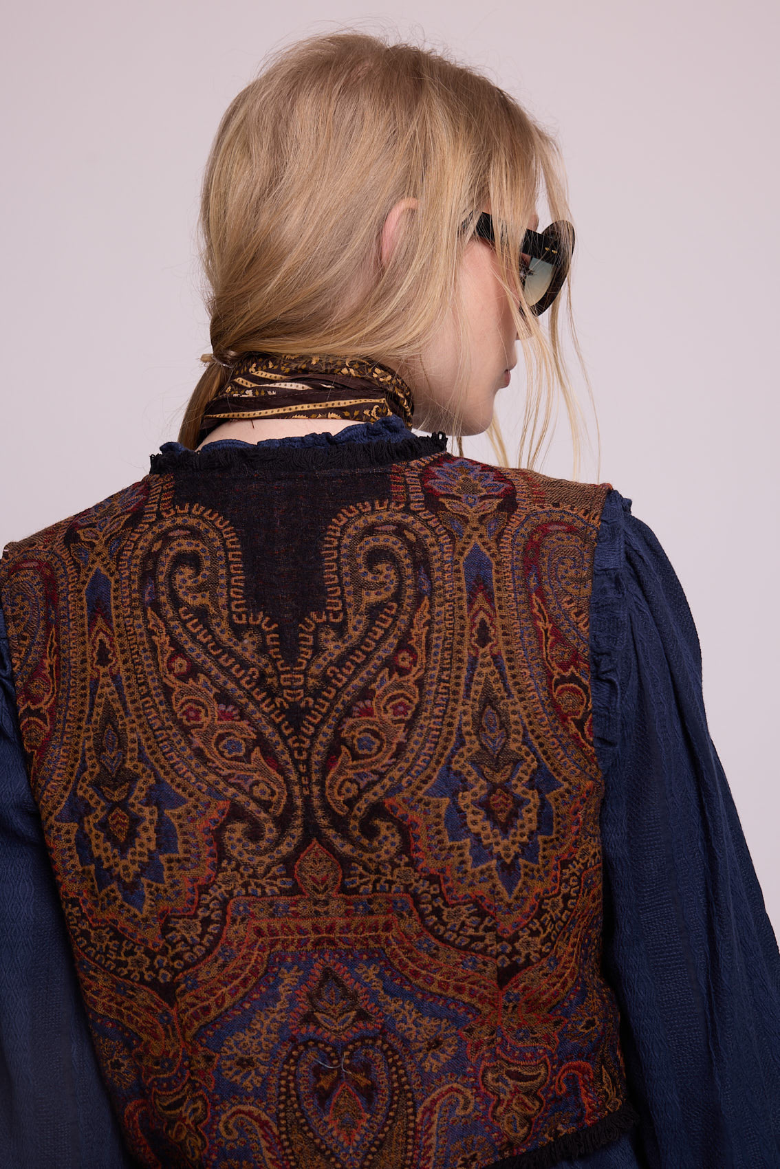 Close-up of model wearing Kleed Blue Oak Vest in pure wool with paisley print, sunglasses and silk scarf at the neck.