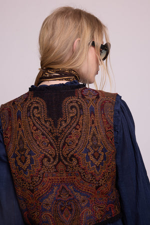 Close-up of model wearing Kleed Blue Oak Vest in pure wool with paisley print, sunglasses and silk scarf at the neck.
