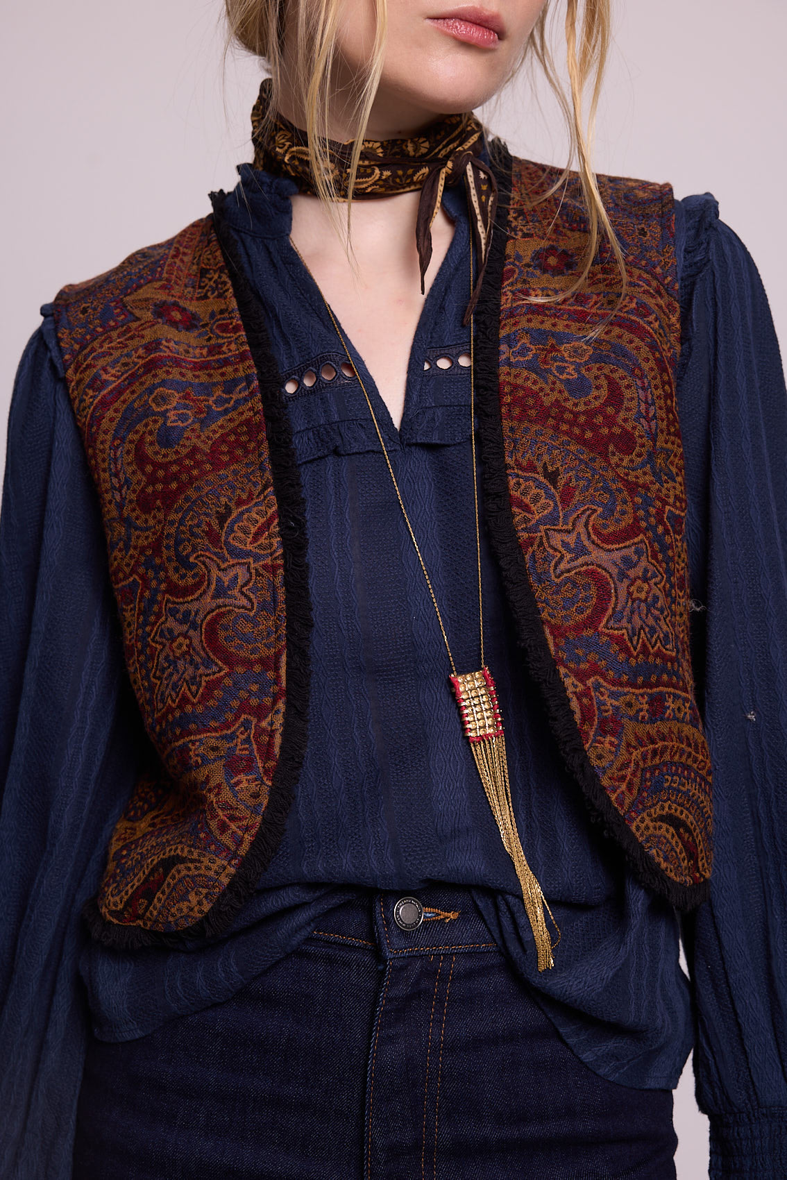 Close-up of model wearing Kleed Blue Oak Vest in wool with paisley swirls, layered over a navy blouse with a long pendant.
