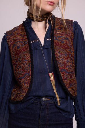 Close-up of model wearing Kleed Blue Oak Vest in wool with paisley swirls, layered over a navy blouse with a long pendant.