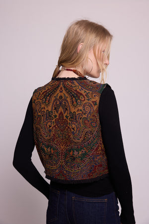 Model from behind wearing Kleed Green Oak Vest in pure wool with paisley print, styled over a black top and dark jeans.