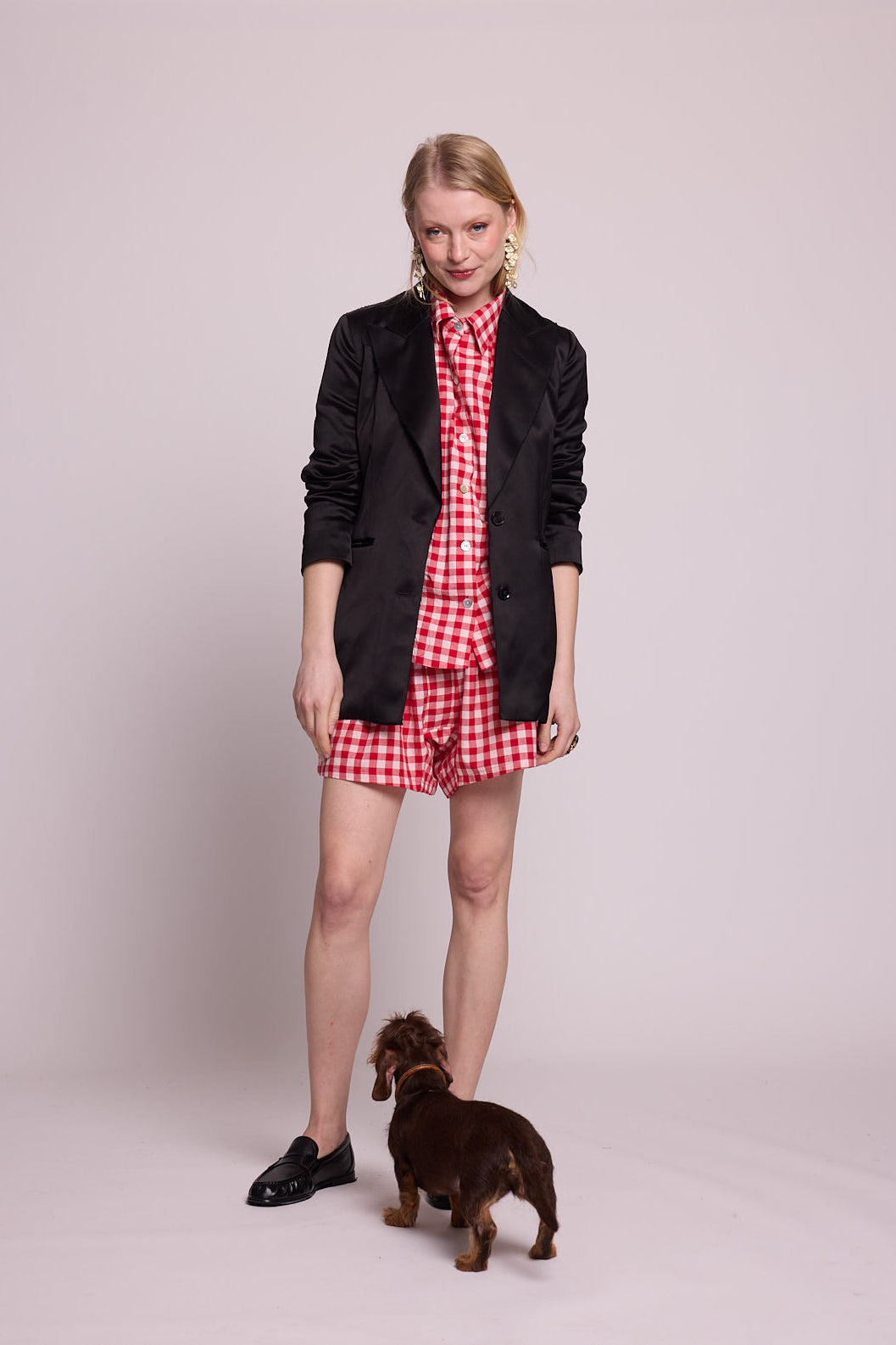 Full length view of a woman wearing the Kleed Bhati Red Pyjama Set in red vichy cotton styled with a black blazer, with a dog at her feet
