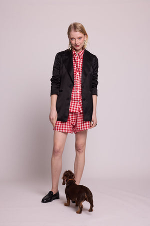Full length view of a woman wearing the Kleed Bhati Red Pyjama Set in red vichy cotton styled with a black blazer, with a dog at her feet