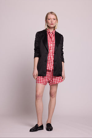 Full length front view of a woman wearing the Kleed Bhati Red Pyjama Set in red vichy cotton styled with a black blazer, black loafers and gold statement earrings
