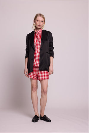 Full length front view of a woman wearing the Kleed Bhati Red Pyjama Set in red vichy cotton styled with a black blazer, black loafers and gold statement earrings, neutral expression