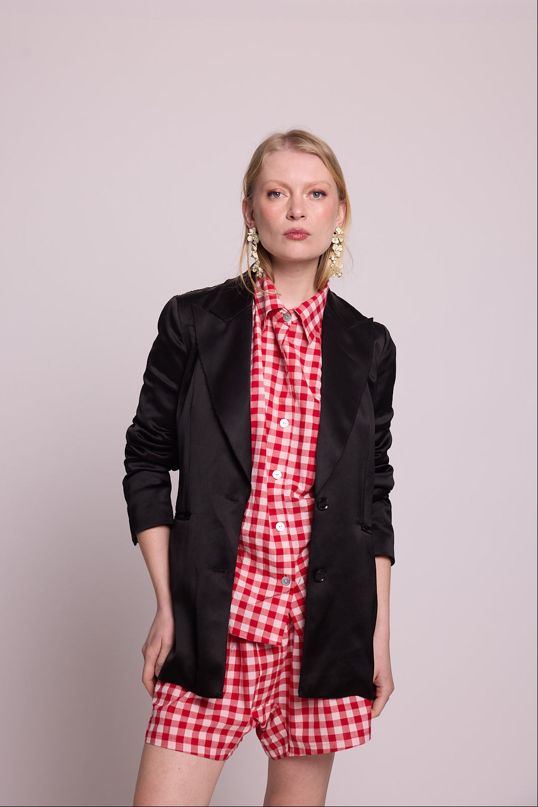 Woman wearing a black blazer over a kleed's bathi red pyjama in red and white checks on a plain background