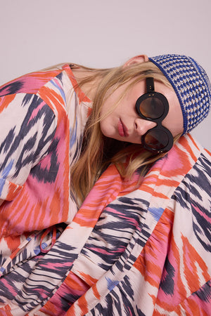 Close up of a woman wearing the Kleed Tangerine Bikaner Maxi Dress in handloomed cotton ikat, styled with a blue ikat cap and round sunglasses