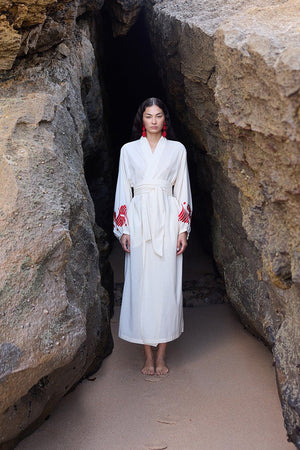 Woman wearing Kleed Natural Kandy Kimono in 100% cotton ivory white with red floral embroidered cuffs standing in cave rocks