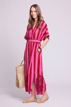Model wearing the Kleed Strawberries Kaftan in pink and red striped 100% cotton, hand block printed and finished with silk embroidery, with side pockets and matching belt, styled with a woven straw hat, oversized straw bag and flat woven shoes.