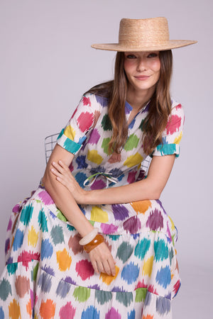 Model seated wearing the anouk maxi dress by kleed in 100% cotton ikat, colourful geometric motifs and some bracelets and straw hat.