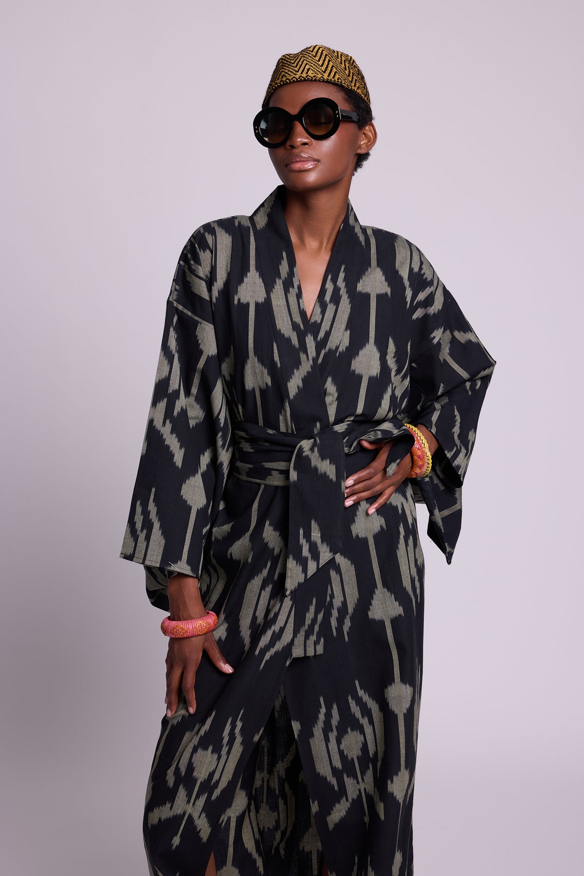 Woman wearing a black and khaki icotton ikat kimono by kleed produced in handlooms with sunglasses and a crochet mustard and black hat and colourful bangles