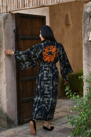 Woman wearing Kleed Congo Naya Kimono in handloomed Ikat cotton black and khaki abstract pattern opening wooden door