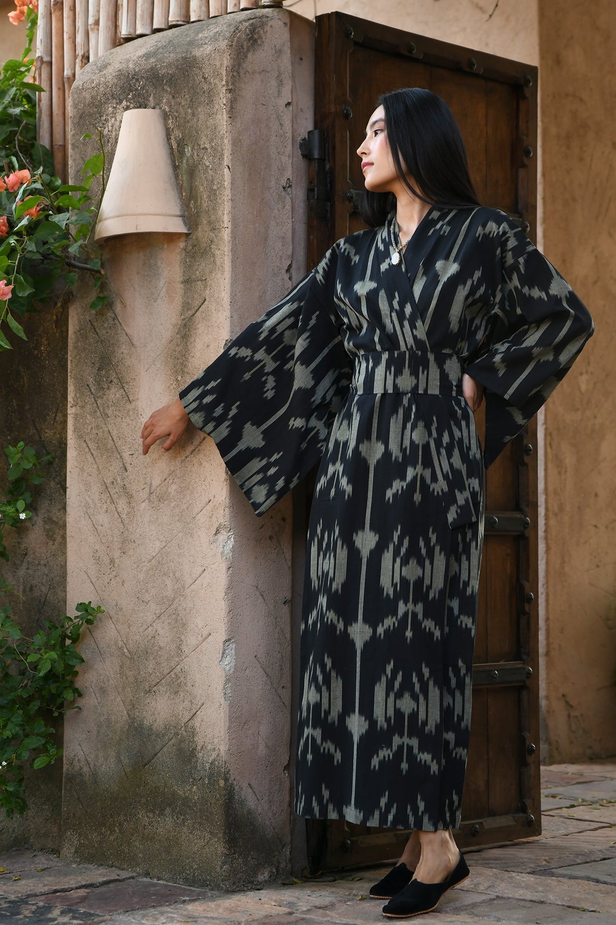 Woman wearing Kleed Congo Naya Kimono in handloomed Ikat cotton black and khaki pattern leaning against wall outdoor