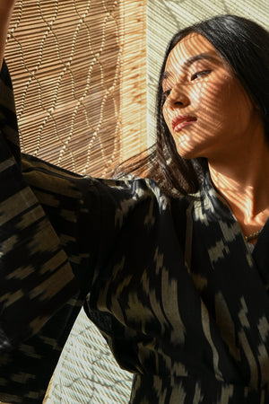 Woman in sunlight wearing Kleed Congo Naya Kimono in handloomed Ikat cotton black and khaki artisanal sustainable kimono