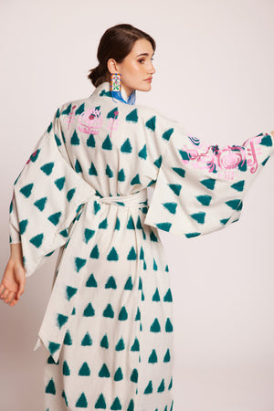 Woman wearing a white kimono with emerald triangle patterns embroidered in pink on a plain background