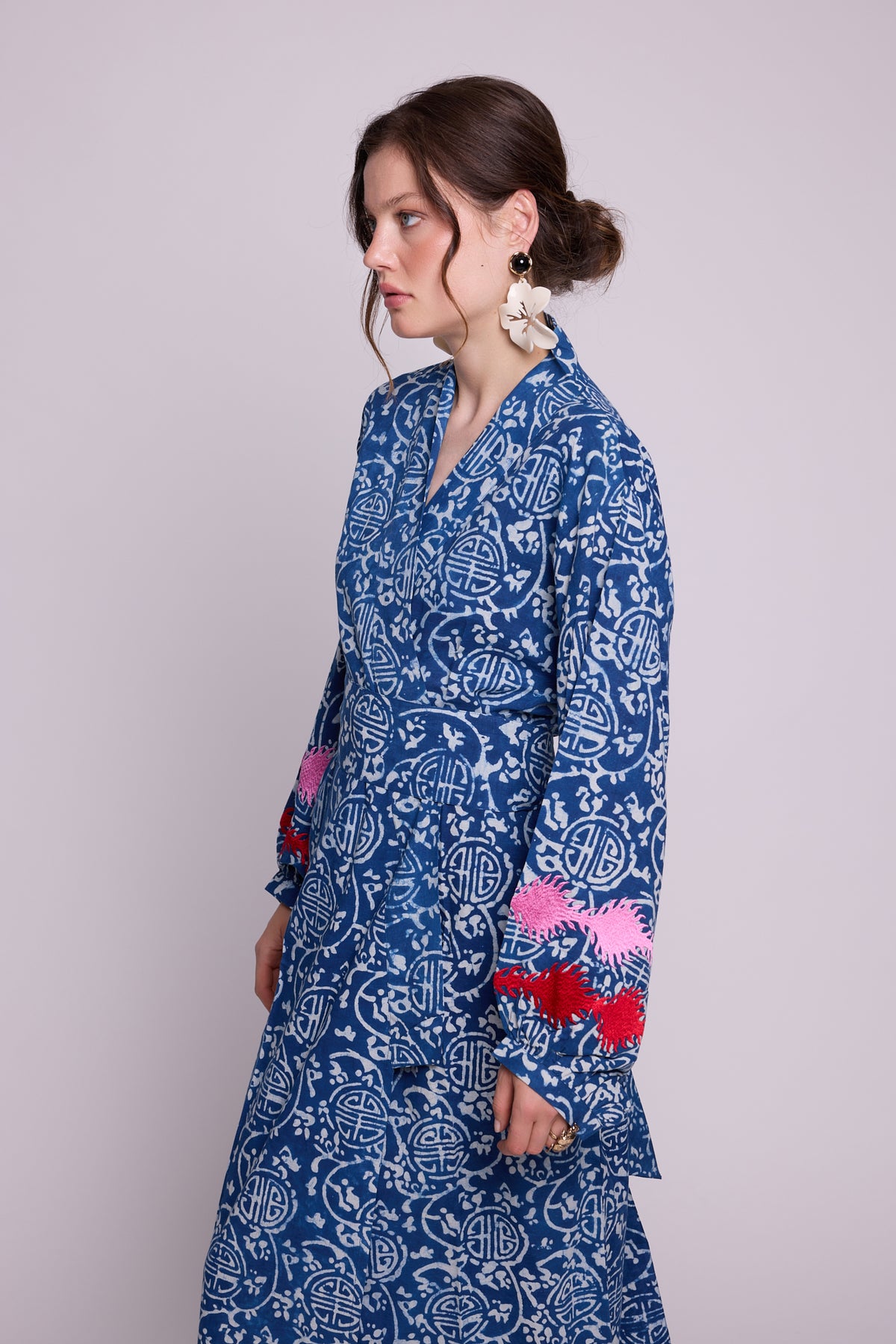 Side view of a woman wearing KLEED’s limited-edition Indira Bloom Kimono, hand block printed in chemical-free indigo blue and white cotton, with pink and red embroidered balloon sleeves and a matching waist belt.